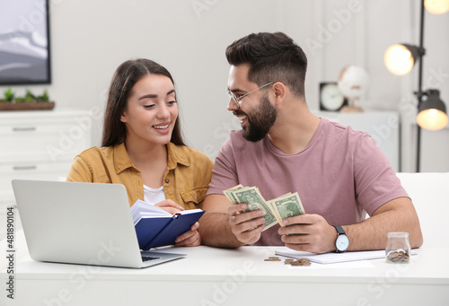 Happy young couple counting money at white table indoors © New Africa