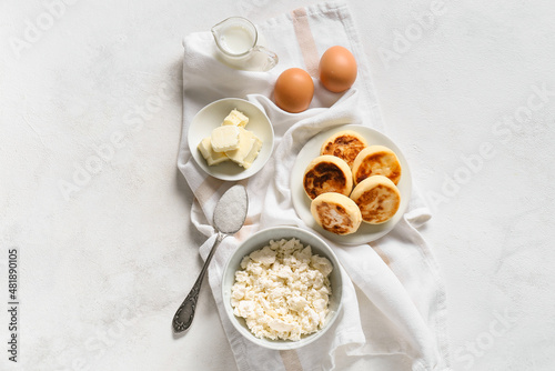 Plate with tasty cottage cheese pancakes and ingredients on white background