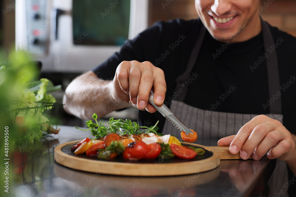 Professional chef decorating cooked dish in restaurant kitchen, closeup