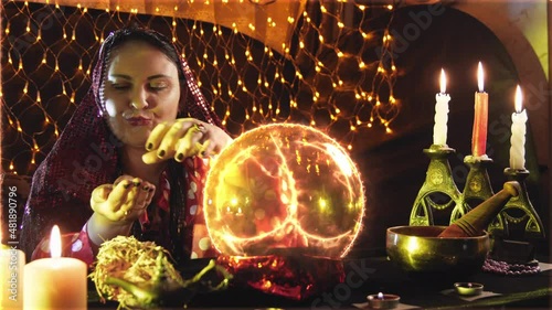 A young sorceress is engaged in magic, reading fate from a small ball by candlelight.