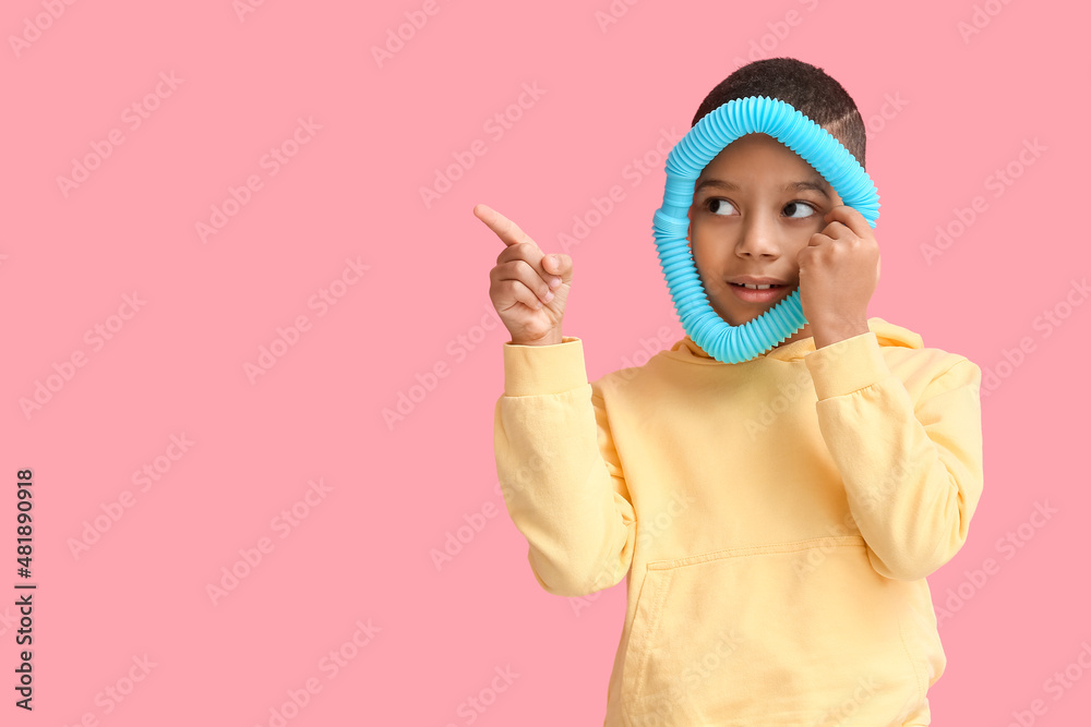 Little African-American boy with blue Pop Tube pointing at something on pink background Little African-American boy with blue Pop Tube pointing at something on pink background