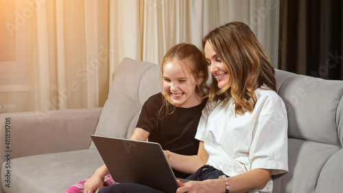 Happy mother and teen daughter in black and white t-shirts watch funny photos on laptop laughing on sofa in living room at home, close view.