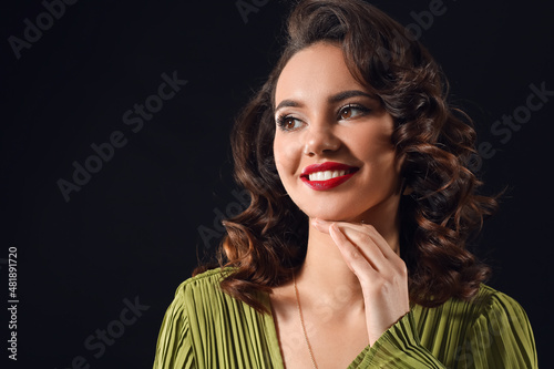 Smiling woman with hand near face looking aside on dark background