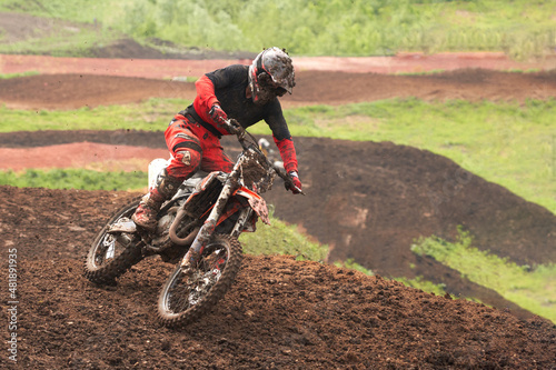 An athlete on a motorcycle rushes along a dirt track. The motorcycle and its equipment are in the mud. Selective focus.