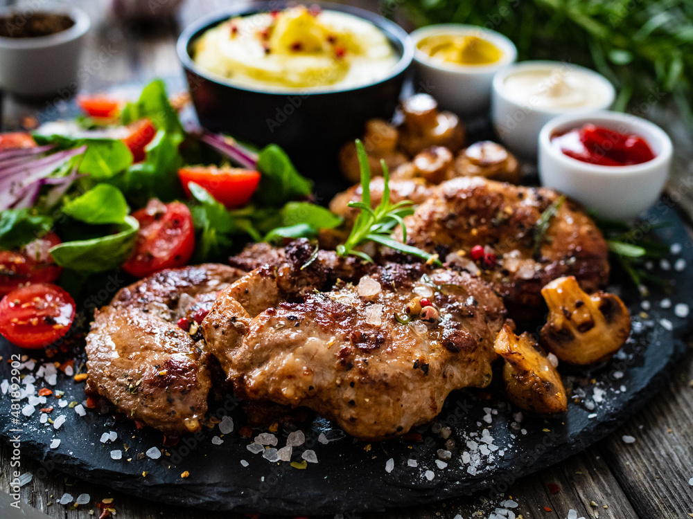 Fried pork steaks with potato puree and vegetable salad served on black stone plate on wooden table
Fried pork steaks with potato puree and vegetable salad served on black stone plate on wooden table