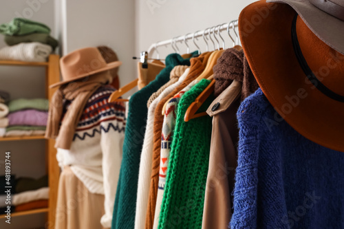 Rack with warm sweaters and hats in dressing room, closeup