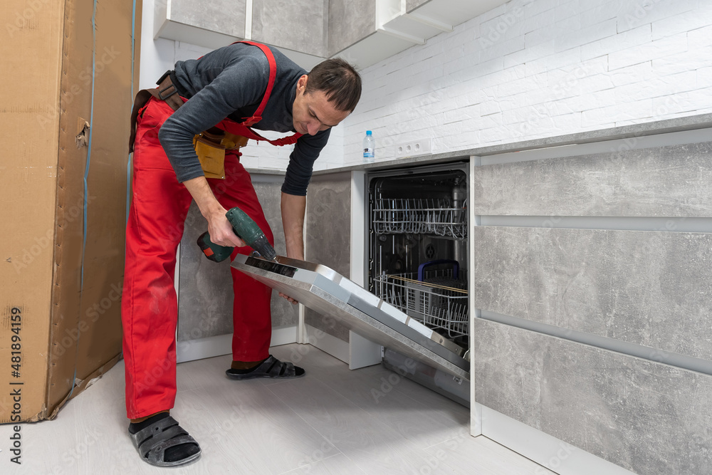 Fototapeta premium Young Repairman Service Worker Repairing Dishwasher Appliance In Kitchen.