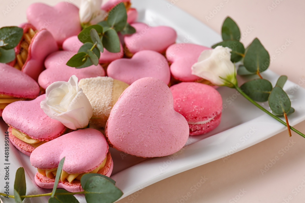 Plate with tasty heart-shaped macaroons and flowers on beige background, closeup Plate with tasty heart-shaped macaroons and flowers on beige background, closeup