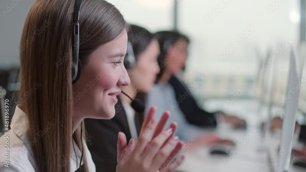 Close Up Portrait Woman of a Technical Customer Support Specialist Talking on a Headset while Working on a Computer in a Call Center. Diverse group of workers talks on sale hotline. Busy seller at
