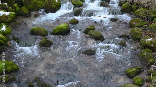 Water flowing in beautiful nature. Rocks covered with green moss and white snow. Idyll winter landscape. Small stream cascading on rocks. Loop video. Fresh nature. Static shot, real time