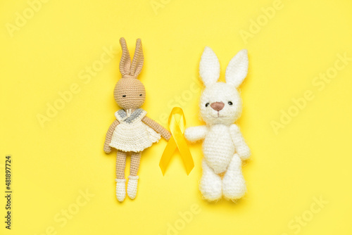 Toy rabbits with golden awareness ribbon on yellow background. International Childhood Cancer Day