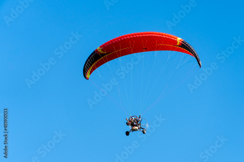 View from below of a paramotor vehicle flying over a clear blue sky