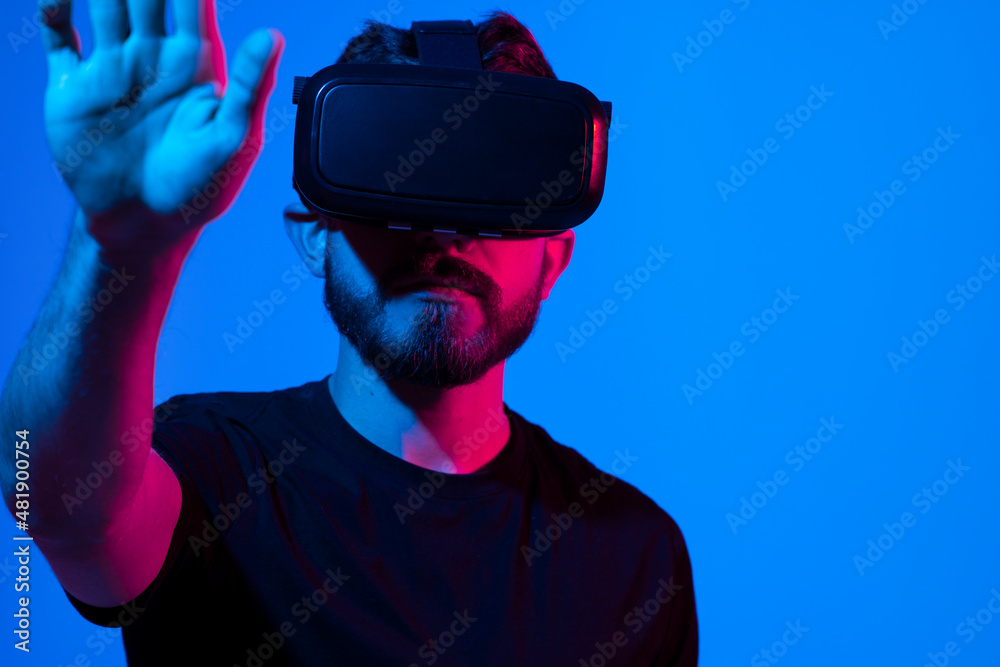 Augmented reality and virtual reality world. Excited bearded guy in vr glasses, touching virtual button while playing video game in goggles, standing in neon light over purple background. Augmented reality and virtual reality world. Excited bearded guy in vr glasses, touching virtual button while playing video game in goggles, standing in neon light over purple background.