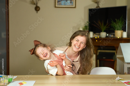 Portrait happy smile family. Mom and daughter at table look at cameras. two sisters laugh At home room and laugh. Place for text. childhood. Caucasian woman and girl in frame. Nanny child Babysitter.