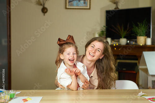Portrait happy smile family. Mom and daughter at table look at cameras. two sisters laugh At home room and laugh. Place for text. childhood. Caucasian woman and girl in frame. Nanny child Babysitter.