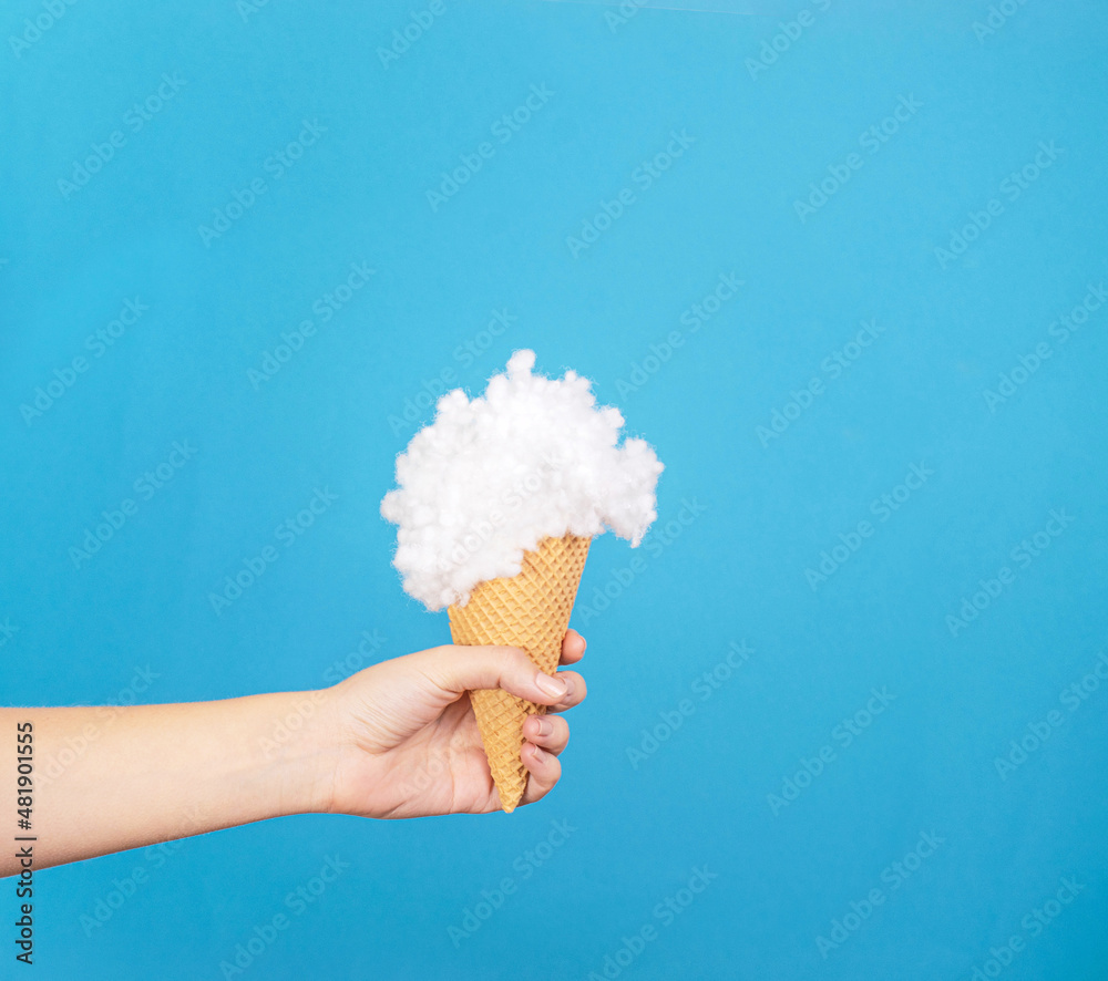 Woman's hand, ice cream and fluffy cloud, creative summer holiday inspired arrangement against bright blue background. Woman's hand, ice cream and fluffy cloud, creative summer holiday inspired arrangement against bright blue background.