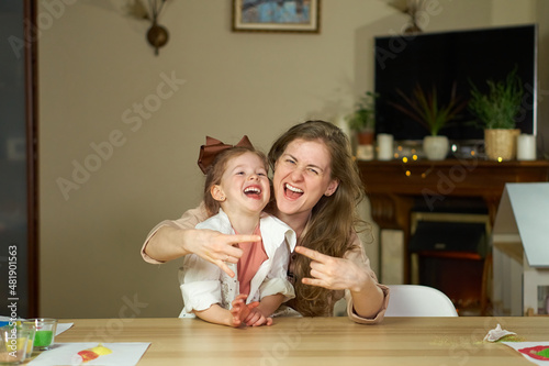 Portrait happy smile family. Mom and daughter at table look at cameras. two sisters laugh At home room and laugh. Place for text. childhood. Caucasian woman and girl in frame. Nanny child Babysitter.