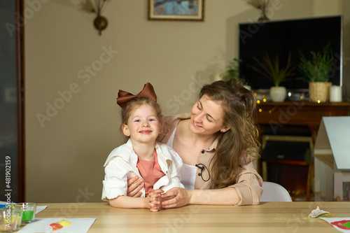 Portrait happy smile family. Mom and daughter at table look at cameras. two sisters laugh At home room and laugh. Place for text. childhood. Caucasian woman and girl in frame. Nanny child Babysitter.