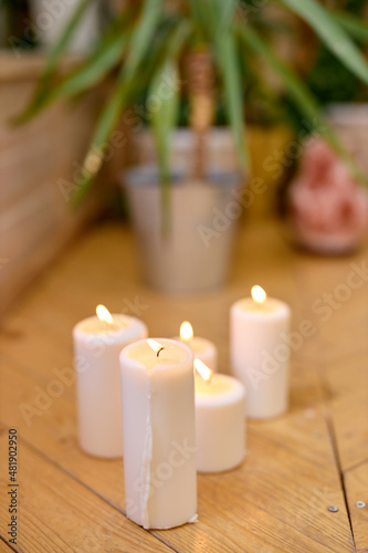 Close-up photo of candles on wooden floor at home  plant in pot in the background. Room with candles for yoga training  calm and beautiful view. No people. copy space