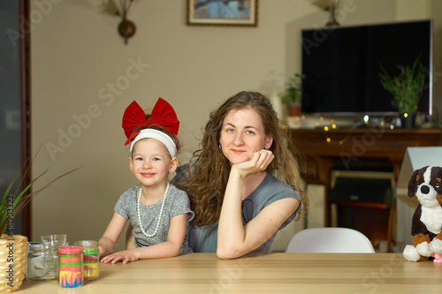Portrait happy smile family. Mom and daughter at table look at cameras. two sisters laugh At home room and laugh. Place for text. childhood. Caucasian woman and girl in frame. Nanny child Babysitter.