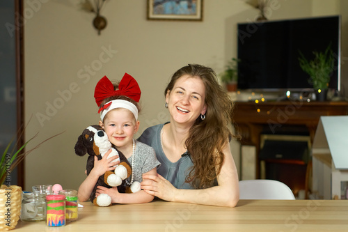 Portrait happy smile family. Mom and daughter at table look at cameras. two sisters laugh At home room and laugh. Place for text. childhood. Caucasian woman and girl in frame. Nanny child Babysitter.