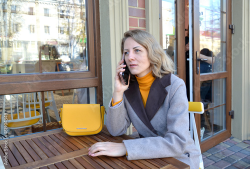 A woman talks on the phone, sitting at the table of a street cafe photo