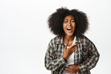 Portrait of beautiful carefree african woman, laughing and smiling joyful, watching smth funny, standing over white background