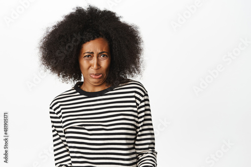 Portrait of Black woman staring with aversion and dislike, cringe from smth bad, awful disgusting taste, standing over white background