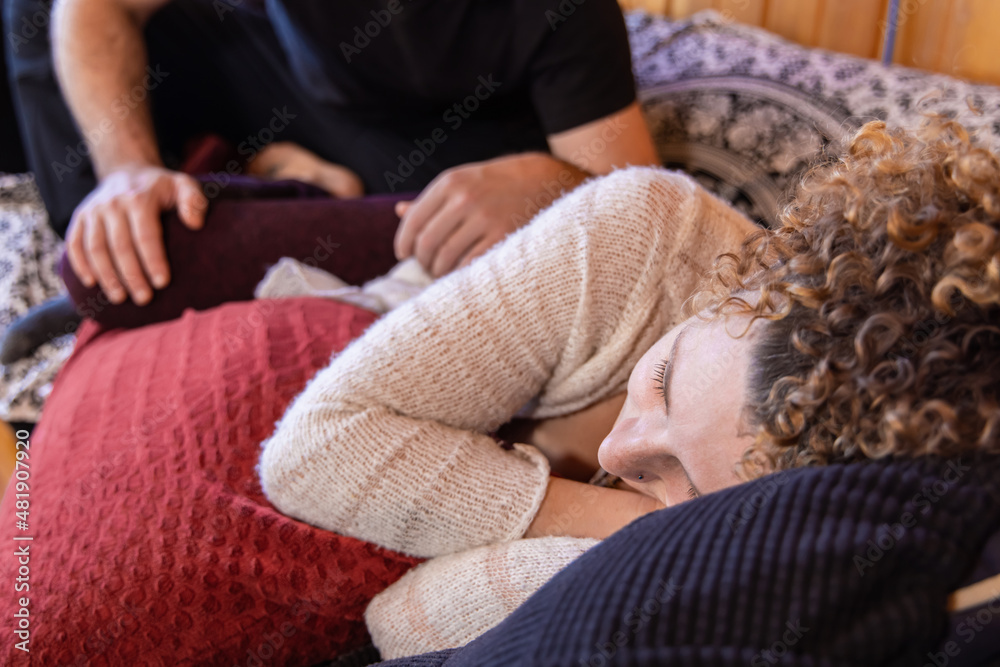 Selective focus shot on the head of a woman seen lying on her side, as a blurry Shiatsu therapist is seen in background massaging upper leg and hip. Selective focus shot on the head of a woman seen lying on her side, as a blurry Shiatsu therapist is seen in background massaging upper leg and hip.