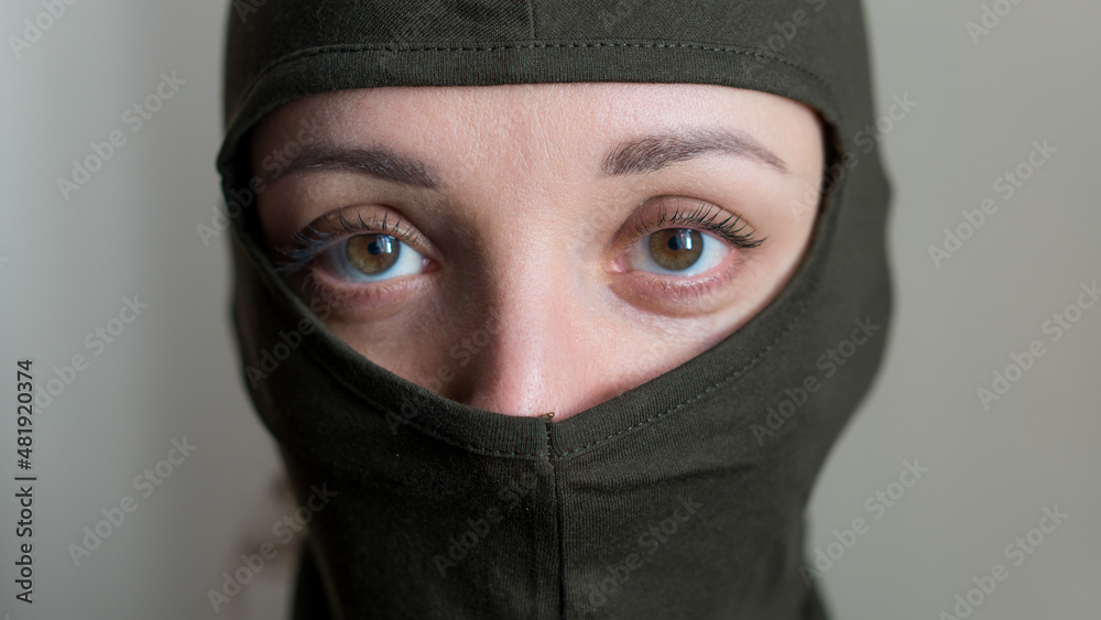 Female portrait of young girl wearing khaki balaclava, only eyes are visible, mandatory conscription, military, feminism, equality concept Female portrait of young girl wearing khaki balaclava, only eyes are visible, mandatory conscription, military, feminism, equality concept