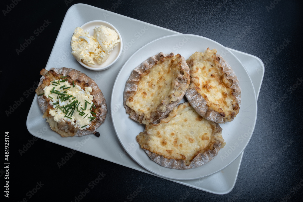 Traditional Finnish foods - Fresh Karelian pies with rice pudding filling and egg butter and chives topping against black background. - obrazy, fototapety, plakaty 