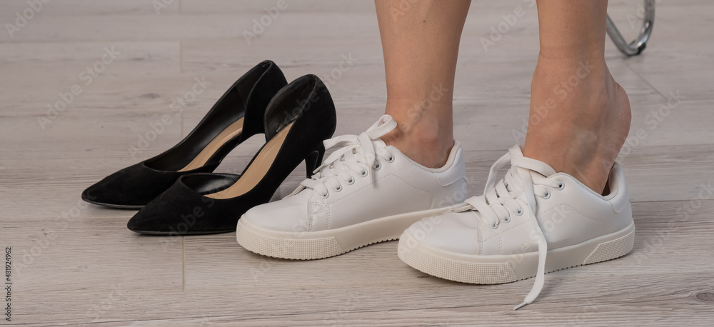 Close-up business woman takes off her shoes puts on white leather sneakers.