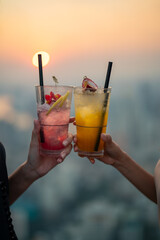 Beautiful Asian woman friends meeting and drinking cocktail together at skyscraper rooftop restaurant in metropolis at summer sunset. Female friend enjoy outdoor lifestyle activity in the city at nigh