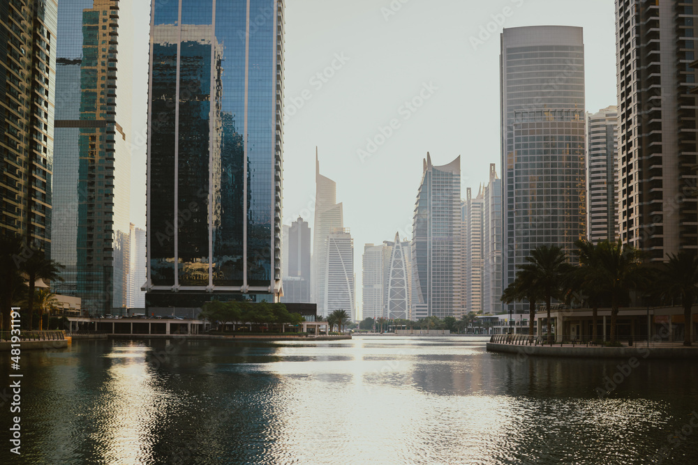 Fototapeta premium Modern city skyscrapers buildings at sunset time with business and residential towers around the lake and palm trees