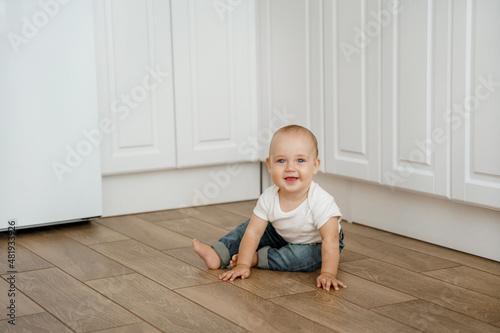 a toddler in a T-shirt and jeans is sitting on the kitchen floor