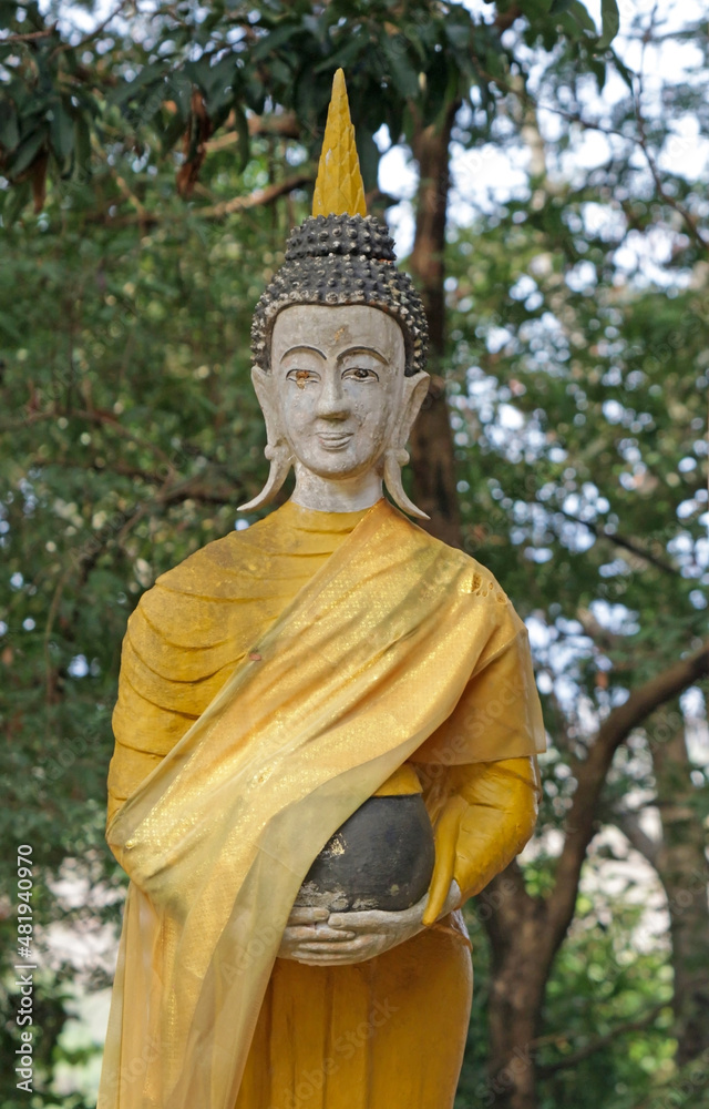 Anceint golden Buddha statue wrapped in cloth and holding a black bowl. Forest trees blurred in background. Anceint golden Buddha statue wrapped in cloth and holding a black bowl. Forest trees blurred in background.