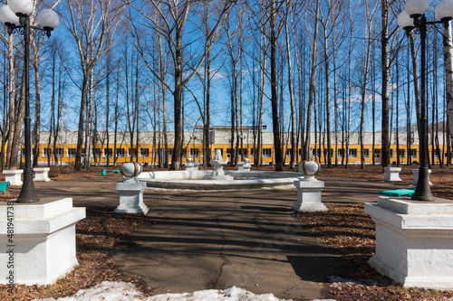 city ​​park with white fountain. vacation in the city in spring. blue sky, trees without leaves in the park