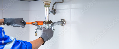 Foto Technician plumber using a wrench to repair a water pipe under the sink