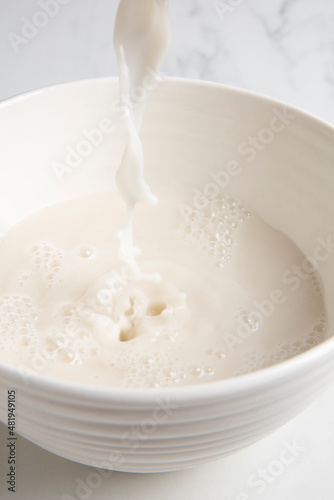 Nut milk bag squeezing milk into a white bowl with almond milk placed on a white marble surface