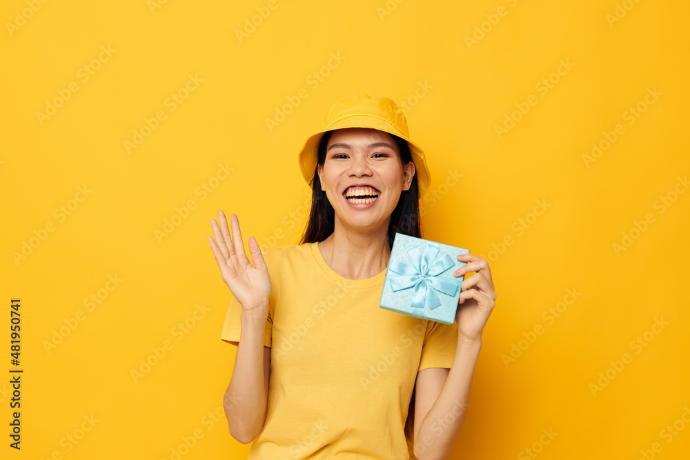 Charming young Asian woman in a yellow T-shirt and a hat with a gift studio model unaltered