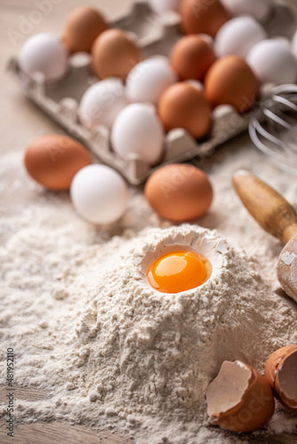 Egg yolk on top of a pile of flour with more eggs and egg shells in preparation of dough for pasta or baking