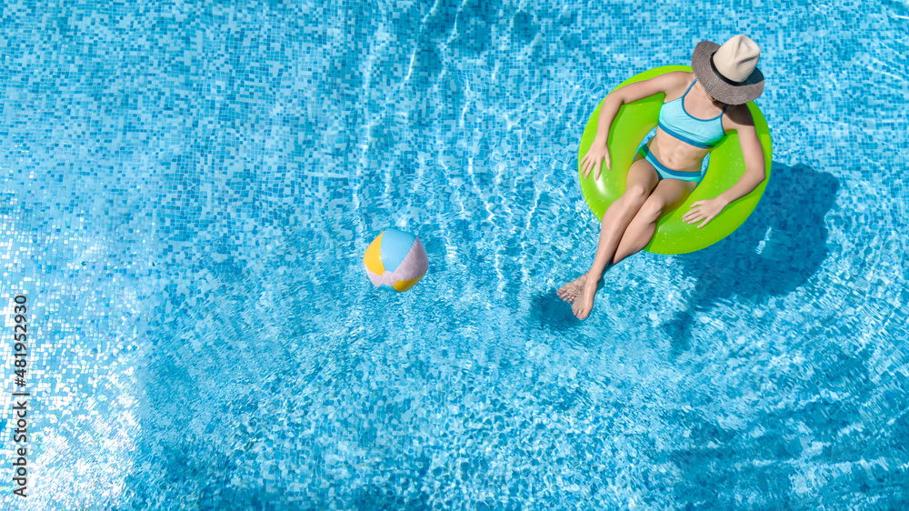 Active young girl in swimming pool aerial top view from above, child relaxes and swims on inflatable ring donut and has fun in water on family vacation, tropical holiday resort