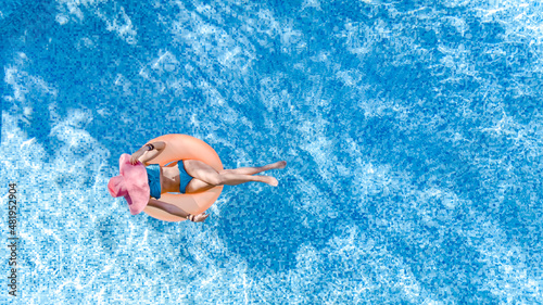 Beautiful woman in hat in swimming pool aerial top view from above, young girl in bikini relaxes and swims on inflatable ring donut and has fun in water on family vacation, tropical holiday resort