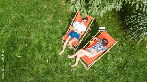 Valokuva Young girls relax in summer garden in sunbed deckchairs on grass, women friends