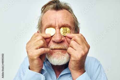 Senior grey-haired man in a blue shirt bitcoins on the face isolated background