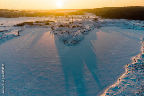 Frozen and snow-covered pond in winter against the backdrop of a bright sunset