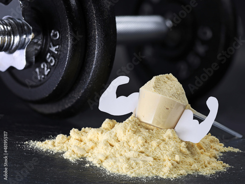 Whey protein scoop with mucles on powder heap with dumbbell on black background, muscle gain from protein shakes photo