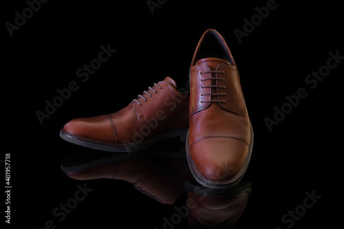 Pair of unbranded brown genuine leather men’s shoes on black reflective surface. Product photography and shopping concept