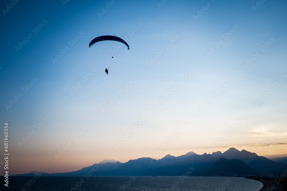 Silhouette of a man on a paraglider flying over the sea at sunset.