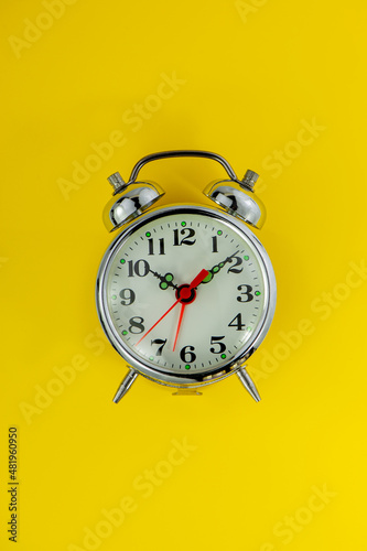 Chromed alarm clock lies on a yellow background.